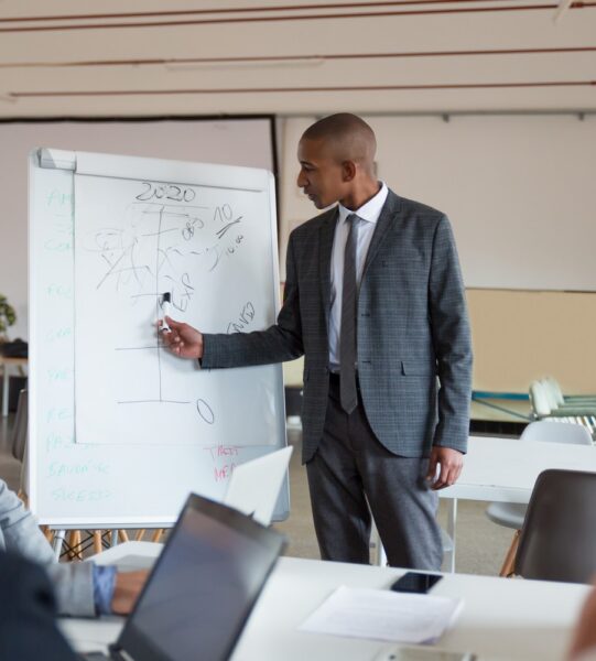Confident speaker talking and pointing at whiteboard. Group of employees discussing ideas during presentation of new project at briefing. Business meeting concept